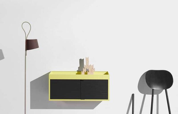 A modern wall-mounted storage unit in bright yellow with black doors and decorative wooden shapes on top.