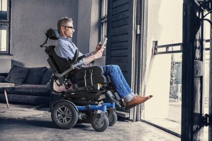 Man seated in a power wheelchair, using a tablet while positioned near an open doorway.