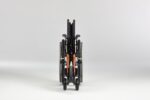 Folded wheelchair with black fabric and orange accents, viewed from the front.