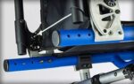 Close-up of blue and black components of a wheelchair frame, showing attachment points and structural elements.