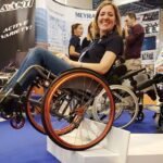 Image: A woman in a wheelchair demonstrates how good the Dezziv Classic Wheelchair Brakes are by balancing on the edge of a step in the wheelchair