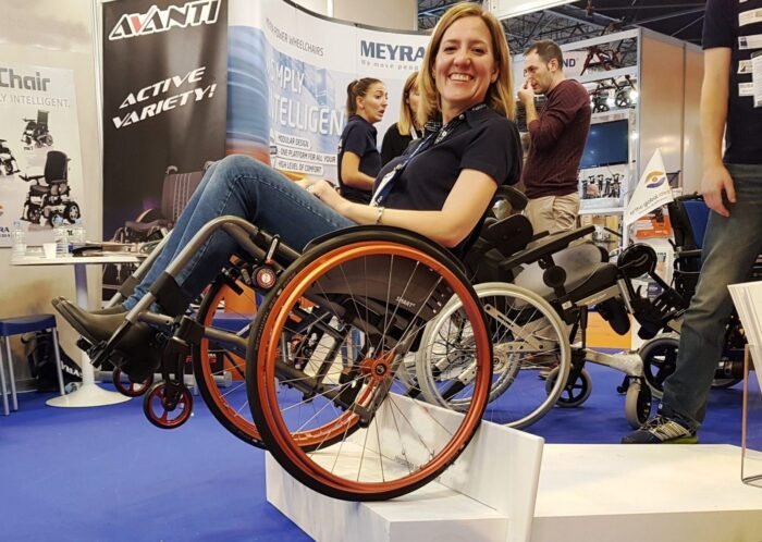 Image: A woman in a wheelchair demonstrates how good the Dezziv Classic Wheelchair Brakes are by balancing on the edge of a step in the wheelchair