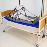 A patient lying on a stretcher sling attached to a hospital bed with safety straps.