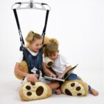 Child safety harness designed with teddy bear features, used by two children reading a book.
