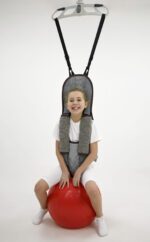 A child smiling while sitting on a red bouncing ball, secured with a support harness.