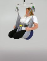 A woman seated in a patient lifting sling suspended from a ceiling lift system.