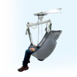 Bariatric fixed lifter with a grey sling and a seated person using it for support.