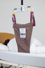 Patient lifting sling attached to a hospital bed with a person lying underneath it.