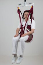A woman seated in a Continental Easy Access Poly patient sling, suspended from a ceiling lift system.