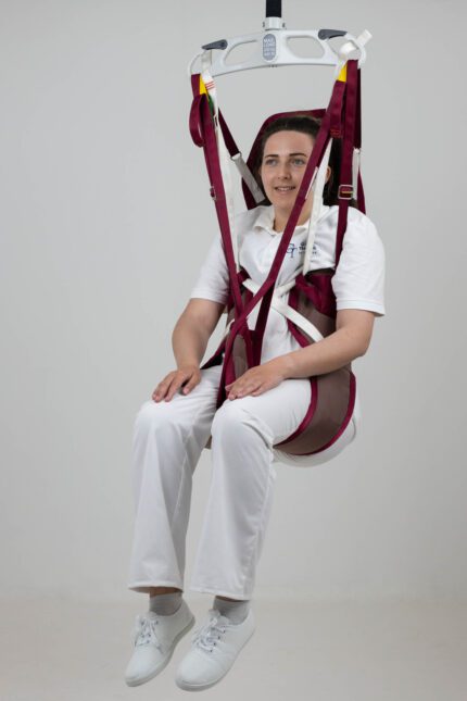 A woman seated in a Continental Easy Access Poly patient sling, suspended from a ceiling lift system.