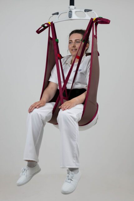 A woman seated in a continental rigid low back poly sling, suspended from a ceiling lift.