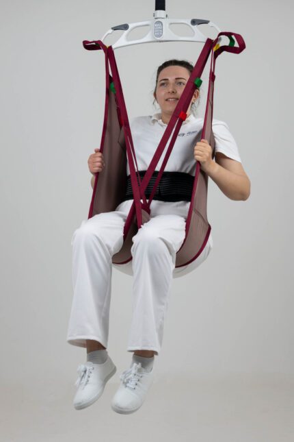 A person seated in a continental rigid low convenience sling, suspended from a lifting device.