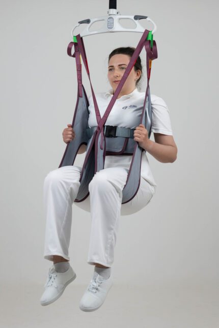 A person seated in a patient sling being lifted by a hoist in a neutral setting.