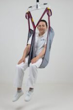 Padded leg sling used for lifting patients, featuring a grey fabric and maroon straps, with a seated model demonstrating its use.