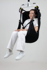 A woman seated in an in-situ recline head support, suspended from a ceiling lift system.