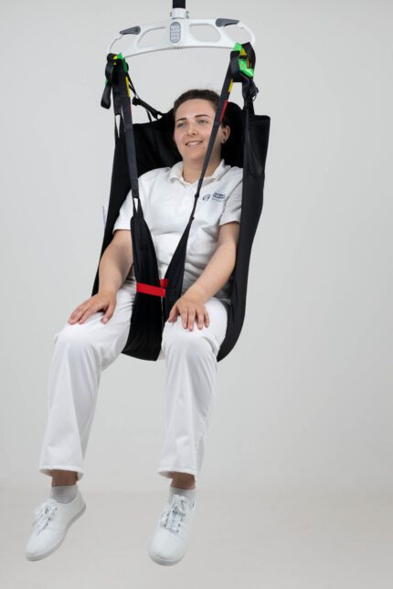 A person seated in an in-situ straight leg head support device, suspended from a ceiling lift.