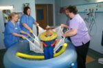 Healthcare professionals assisting a child in a manual birthing sling in a water environment.