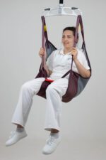 A person seated in a Silva Deluxe patient lifting sling, suspended from a ceiling lift system.