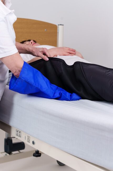 A healthcare professional applying therapeutic compression mitts on a patient lying on a hospital bed.