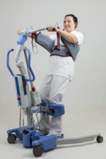 A woman using a stand-up sling lifting device for mobility assistance.