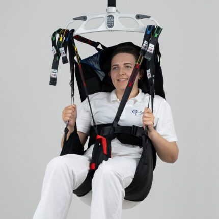 Individual seated in a Tinkham sling, suspended from a ceiling-mounted lift system.